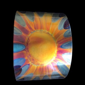 May include: A round, metallic, decorative object with a sun-like design. The center of the object is a bright yellow, surrounded by orange, red, blue, and purple swirls.