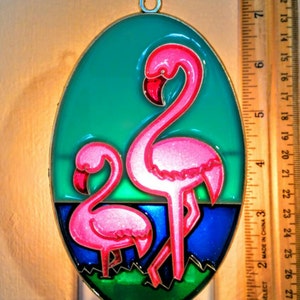 May include: A pink flamingo night light with a smaller flamingo in the foreground. The night light is plugged into an outlet and is lit up. The background is a green, blue, and white design.