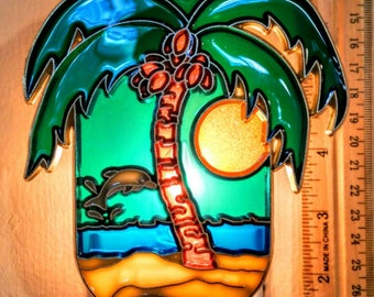 Op de afbeelding: Een nachtlamp van gekleurd glas met een palmboom, een zonsondergang en een dolfijn op de achtergrond. De nachtlamp is aangesloten op een stopcontact.