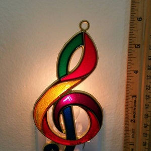 May include: A colorful glass night light shaped like a treble clef. The night light is plugged into an electrical outlet and is lit up.