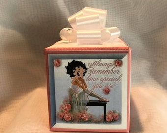 Peut inclure: Une boîte cadeau rose et bleue avec un ruban blanc. La boîte présente une image d'un personnage de dessin animé jouant du piano avec le texte "Always Remember how special you are".