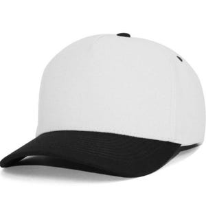 May include: A five-panel baseball cap featuring a solid white crown and a contrasting black curved brim. The cap includes a small black button at the top center and black eyelets for ventilation, providing a clean and structured appearance.