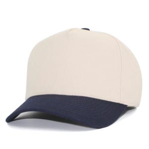 May include: A five-panel baseball cap featuring a solid cream-colored crown and a contrasting dark navy blue curved brim. The structured front panel is plain and unadorned, while the cap maintains a clean, simple design with visible stitching.