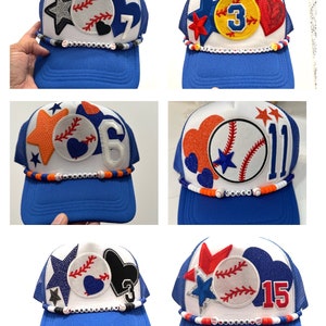 May include: Six blue and white baseball caps with different colored patches and beads. The caps have a mesh back and a white front with a baseball, star, heart, and number patches. The beads are white, orange, red, and black.
