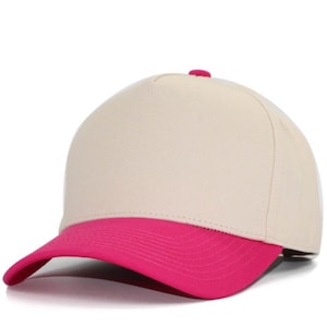 May include: A five-panel baseball cap featuring a solid cream-colored crown and a vibrant hot pink curved brim. The cap includes a small matching hot pink button at the top center, with structured front panels and stitched detailing on the brim.
