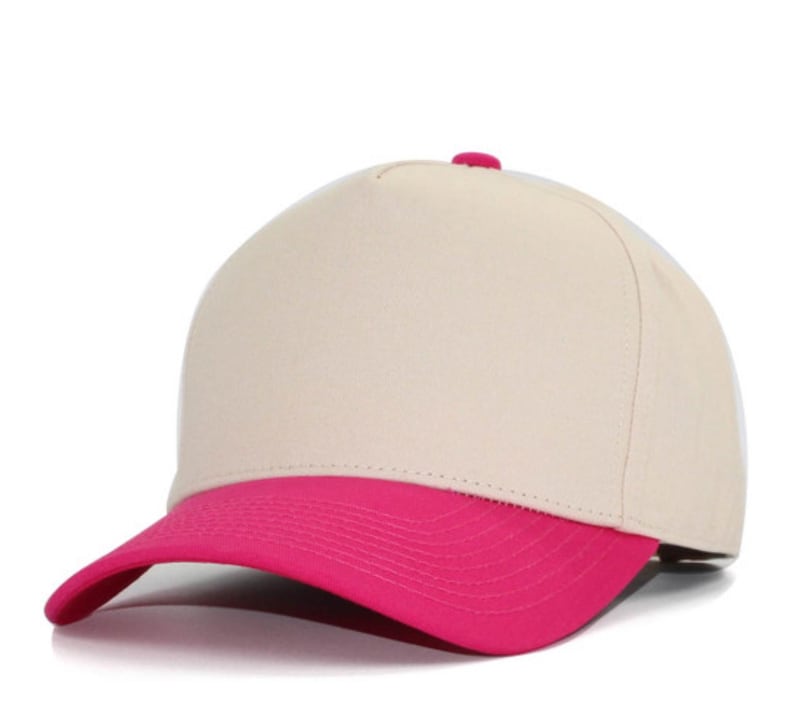 May include: A five-panel baseball cap featuring a solid cream-colored crown and a vibrant hot pink curved brim. The cap includes a small matching hot pink button at the top center, with structured front panels and stitched detailing on the brim.