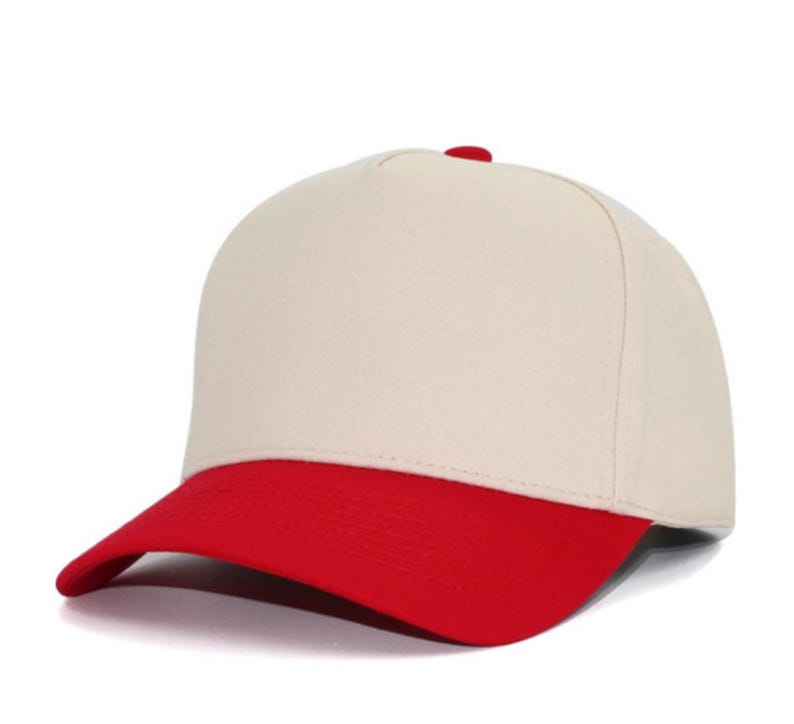 May include: A five-panel baseball cap featuring a solid cream-colored crown and a contrasting bright red curved brim. The cap includes a small red button at the top center where the panels meet, providing a clean and structured appearance.
