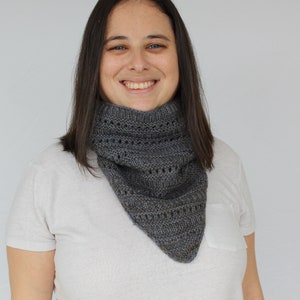 May include: A woman wearing a white t-shirt with a gray knitted cowl neck scarf. The scarf has a lacy pattern.