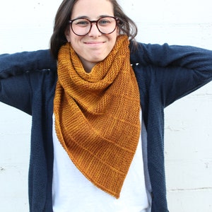 May include: A woman wearing a navy blue cardigan with a mustard yellow knitted scarf. The scarf is triangular in shape and has a textured knit pattern.