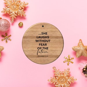May include: A round wooden ornament with the text "...SHE LAUGHS WITHOUT FEAR OF THE future." and "PROVERBS 31:25" on a pink background with gold glitter ornaments.