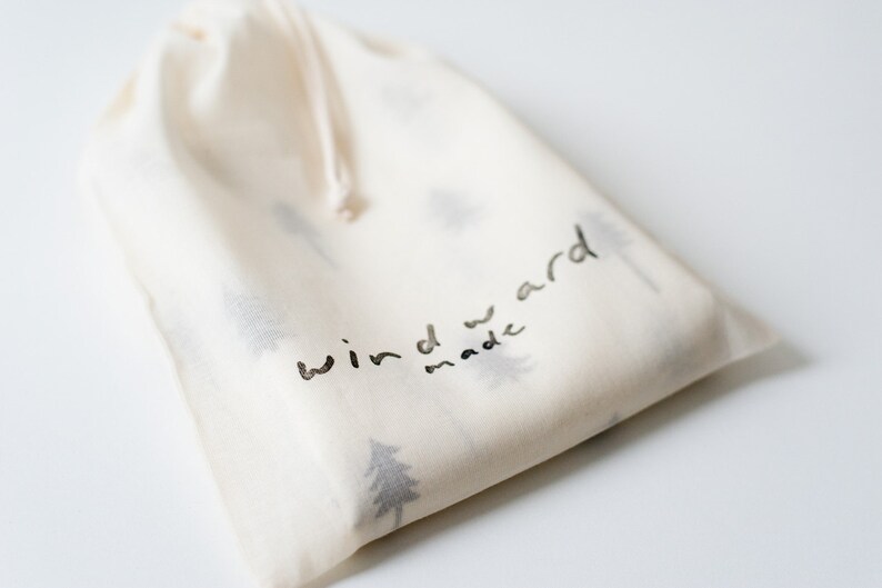 K&ouml;nnte beinhalten: Eine wei&szlig;e Baumwolltasche mit Kordelzug und schwarzem Aufdruck "windward made" sowie einem Muster aus kleinen B&auml;umen.