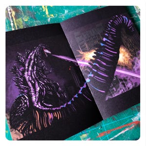 Op de afbeelding: Een zwart en paars ge&iuml;llustreerd boek met een monster op de omslag. Het monster is een groot, reptielachtig wezen met een lange staart en scherpe tanden. Het boek is open op een pagina die een close-up van de staart van het monster laat zien.
