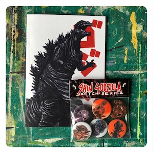 Op de afbeelding: Een zwart-witte illustratie van Godzilla op een witte kaart met rode Japanse karakters. Een plastic zakje met zes kleurrijke knopen met Godzilla in verschillende poses. Het zakje heeft de tekst "Shin Godzilla Sketch Series".