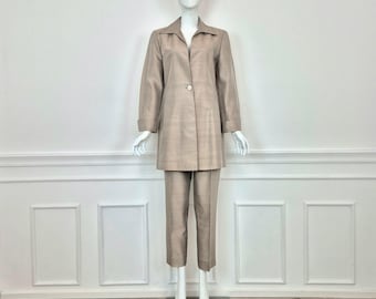 Puede incluir: Un traje de pantalón beige con una chaqueta larga y un cierre de un solo botón. La chaqueta tiene cuello y mangas largas. El pantalón es corto y tiene una pierna recta.