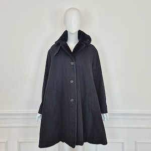 Può includere: Un cappotto nero con colletto e fodera in ecopelliccia, chiusura con bottoni e due tasche anteriori. Il cappotto è esposto su un manichino su sfondo bianco. Il cappotto è uno stile al ginocchio.