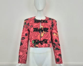 May include: A cropped red jacket with a floral print and black satin bows. The jacket has a fitted silhouette and long sleeves.