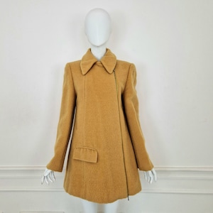 Può includere: Un cappotto di lana giallo senape con chiusura a zip e una sola tasca sul lato sinistro.