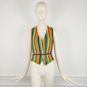 Puede incluir: Un chaleco sin mangas con cuello en V y un estampado de rayas de colores. El chaleco tiene un dobladillo puntiagudo y un cinturón negro.