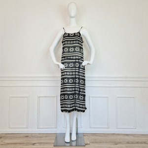 May include: A black and white patterned midi dress with thin straps. The dress has a snowflake design and a black waistband.