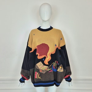 Peut inclure: Pull ample avec un design unique. Le haut est jaune moutarde avec un motif rouge et orange, passant à des manches noires et une partie inférieure marron. Le pull présente un coffre au trésor et un motif de sirène.