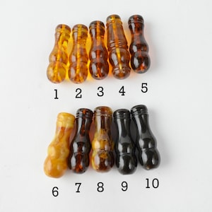 Puede incluir: Diez cuentas de color ámbar y negro en forma de calabaza, numeradas del 1 al 10. Las cuentas están dispuestas en dos filas, con las cuentas de ámbar en la fila superior y las cuentas negras en la fila inferior.