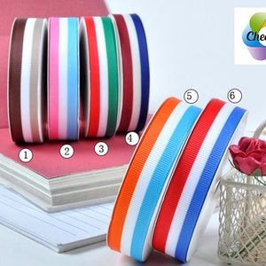 May include: Six rolls of double-sided ribbon with white and a variety of colors, including brown, pink, light blue, red, burgundy, and navy blue. The ribbon is arranged in a row on a stack of notebooks. The ribbon is labeled with numbers 1 through 6.