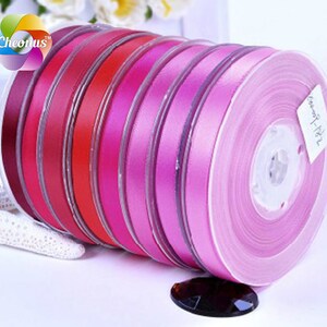 May include: A set of eight spools of satin ribbon in various shades of pink and red. The ribbon is wound around clear plastic spools.