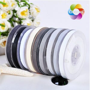 May include: A set of 10 spools of ribbon in various shades of gray, white, and black. The ribbon is wound around spools with clear plastic cases. The spools are arranged in a stack.