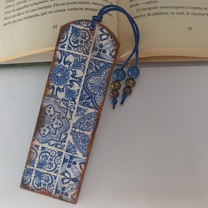 Könnte beinhalten: Ein blaues und weißes gemustertes Lesezeichen mit einem blauen Quasten und Perlen. Das Lesezeichen ist aus Holz und hat eine abgenutzte Oberfläche.