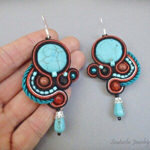 May include: A pair of turquoise and orange earrings with a turquoise stone in the center of each earring. The earrings are made with a variety of beads and cords.