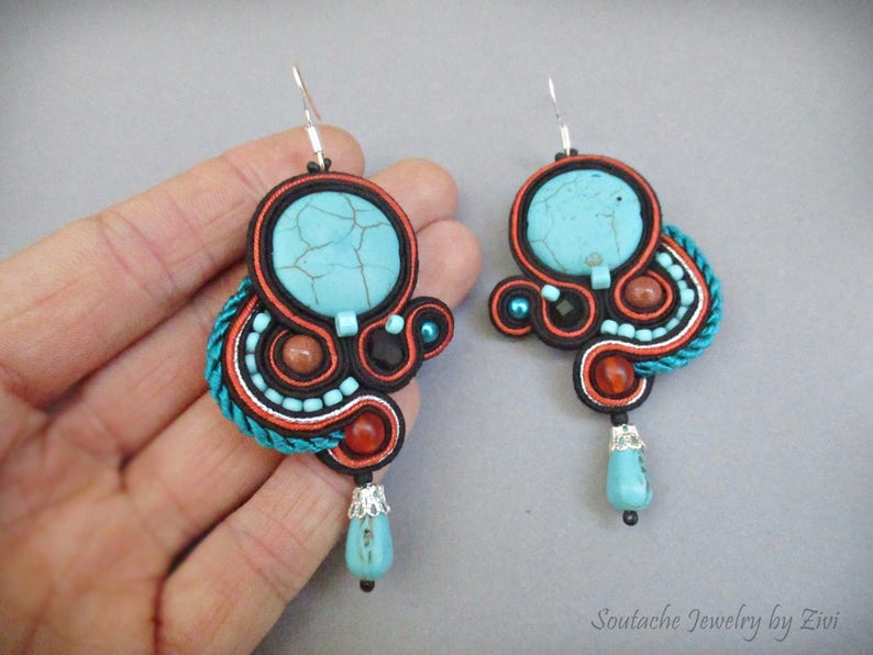 May include: A pair of turquoise and orange earrings with a turquoise stone in the center of each earring. The earrings are made with a variety of beads and cords.