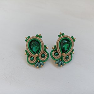 May include: A pair of green and gold earrings with a teardrop-shaped green gemstone in the center of each earring.
