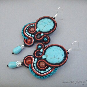 May include: A pair of turquoise and orange earrings with a beaded design. The earrings feature a large turquoise stone and are made with a variety of beads and threads.