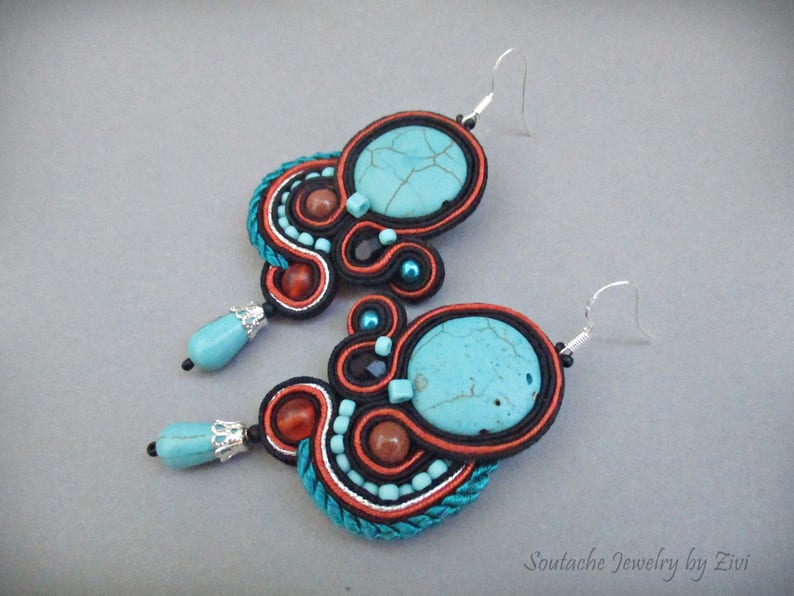 May include: A pair of turquoise and orange earrings with a beaded design. The earrings feature a large turquoise stone and are made with a variety of beads and threads.