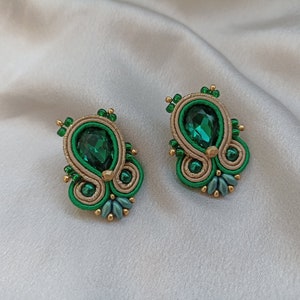 May include: A pair of green and gold earrings with a teardrop-shaped green gemstone in the center of each earring.
