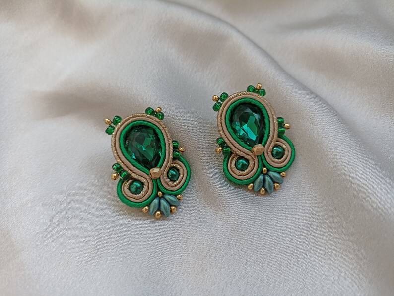 May include: A pair of green and gold earrings with a teardrop-shaped green gemstone in the center of each earring.
