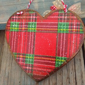 May include: Red, green, and white plaid heart-shaped wooden ornament with a white and red twine hanger and a beige lace bow.