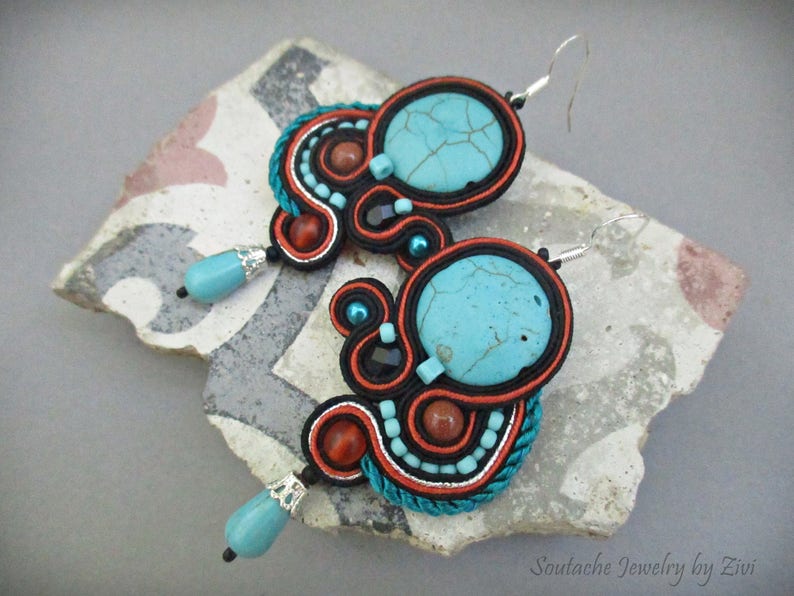 May include: A pair of turquoise and orange earrings with a silver hook closure. The earrings are made with a variety of materials, including beads, wire, and fabric. The earrings are a unique and stylish accessory.