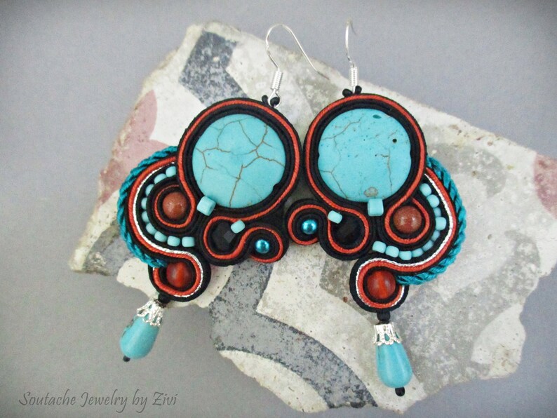 May include: A pair of turquoise and red soutache earrings with a turquoise stone in the center of each earring. The earrings are handmade and feature a silver hook.