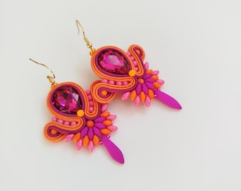 May include: A pair of vibrant, handmade earrings. Each earring features a large, oval, magenta-colored gemstone surrounded by orange and magenta soutache braid. Small pink and orange beads and a magenta teardrop accent complete the design.