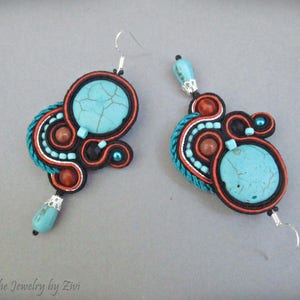 May include: A pair of turquoise and orange earrings with intricate beaded designs. The earrings feature a large turquoise stone in the center of each earring.