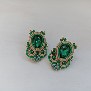 May include: A pair of green and gold earrings with a teardrop-shaped green gemstone in the center of each earring.