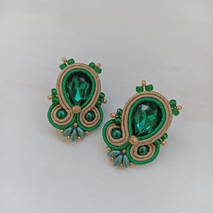 May include: A pair of green and gold earrings with a teardrop-shaped green crystal in the center of each earring.