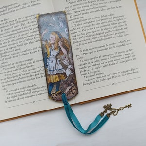 Può includere: Un segnalibro con un'illustrazione vintage di Alice nel Paese delle Meraviglie che tiene un mazzo di carte. Il segnalibro è fatto di carta spessa e ha un nastro turchese. Il testo sul segnalibro dice "You are te convencing of the dignity no se come."