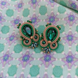 May include: A pair of green and gold earrings with a teardrop-shaped green crystal in the center of each earring.