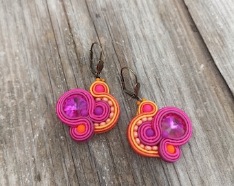 May include: A pair of pink, orange, and yellow earrings with a large pink crystal in the center of each earring.