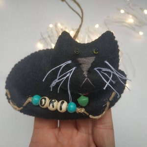 May include: Black felt cat ornament with green felt tongue and turquoise beads spelling "ORI".