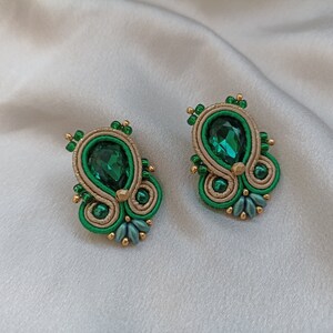 May include: A pair of green and gold earrings with a teardrop-shaped green gemstone in the center.