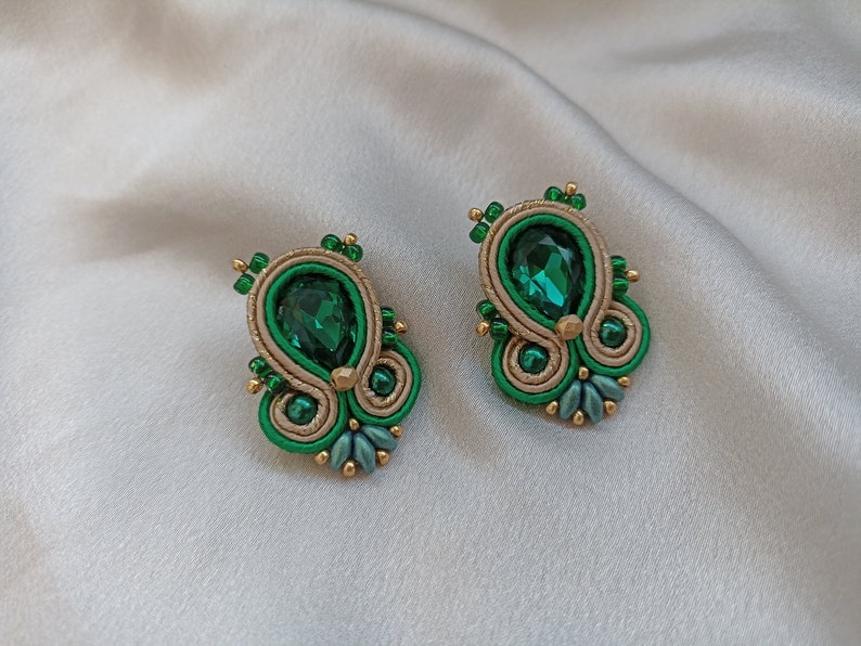 May include: A pair of green and gold earrings with a teardrop-shaped green gemstone in the center.