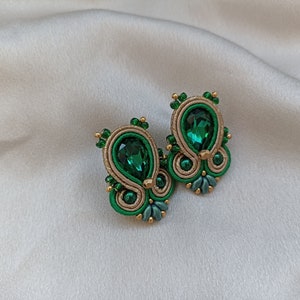 May include: A pair of green and gold earrings with a teardrop-shaped green gemstone in the center of each earring.